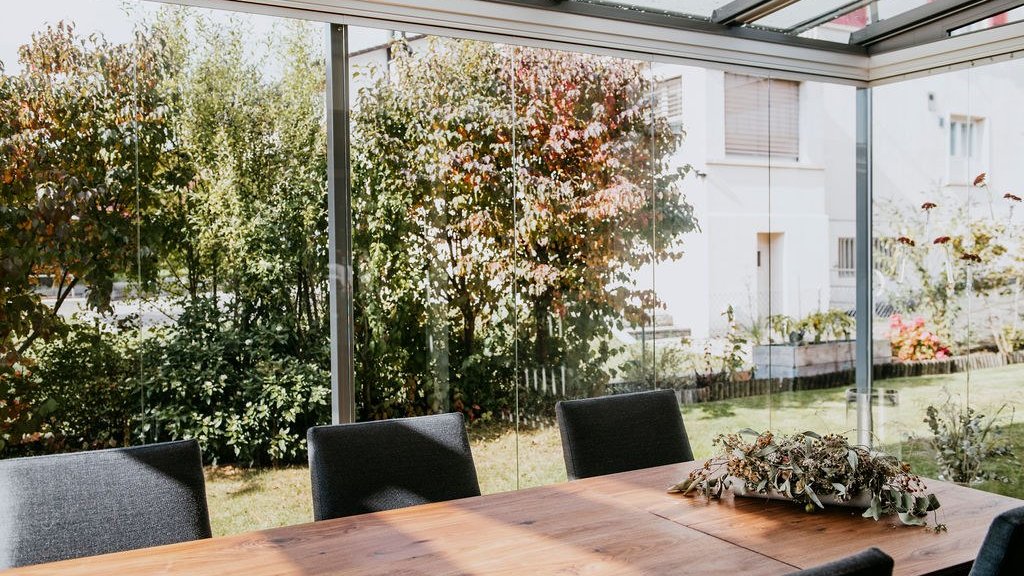 Table à manger dans un jardin d’été avec toit en verre ROOFS et vitrage COVER devant des arbres d’automne