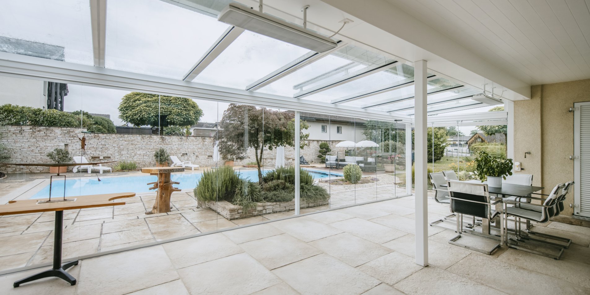 Vitrage de terrasse COVER sous toit en verre ROOFS, avec vue sur le jardin et la piscine, coin repas à droite