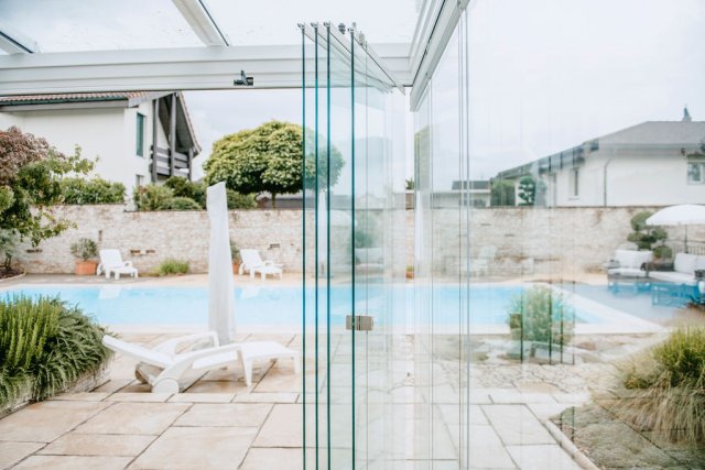 Vitrage coulissant-pivotant COVER ouvert, vantaux en verre regroupés devant une piscine