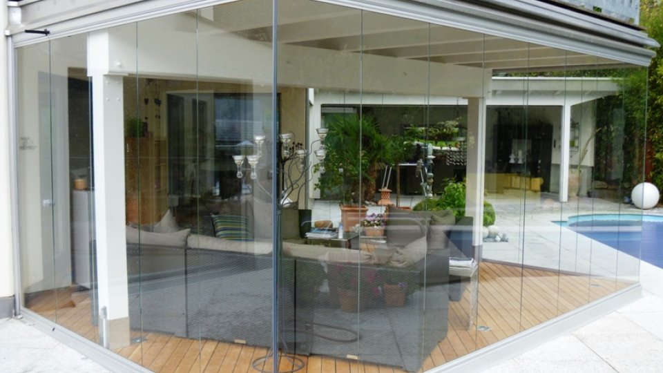 Vetrata d’angolo COVER su una terrazza con pavimento in legno, lounge e piscina sullo sfondo