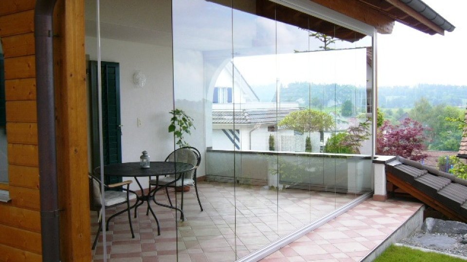 Terrazza vetrata con vetrata scorrevole-girevole COVER, tavolino da bistrot e facciata in legno