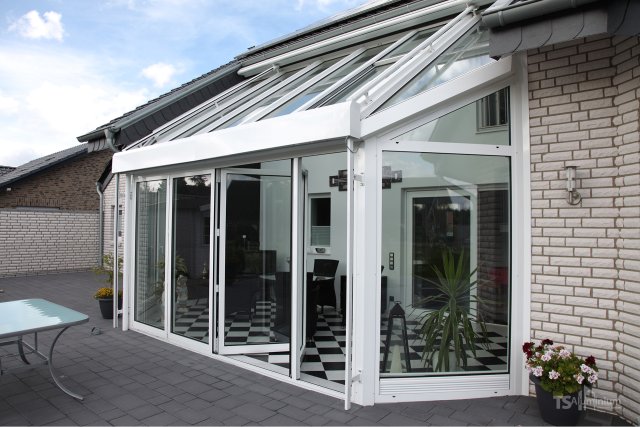 Weisses Glasdach ROOFS mit Faltverglasung FOLDER als Anbau an ein Backsteinhaus auf einer Terrasse
