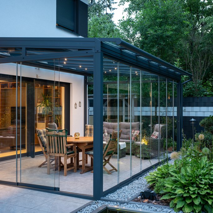 Beleuchteter schwarzer Sommergarten mit Schiebeverglasung SLIDER in der Abenddämmerung, mit Essplatz und Lounge