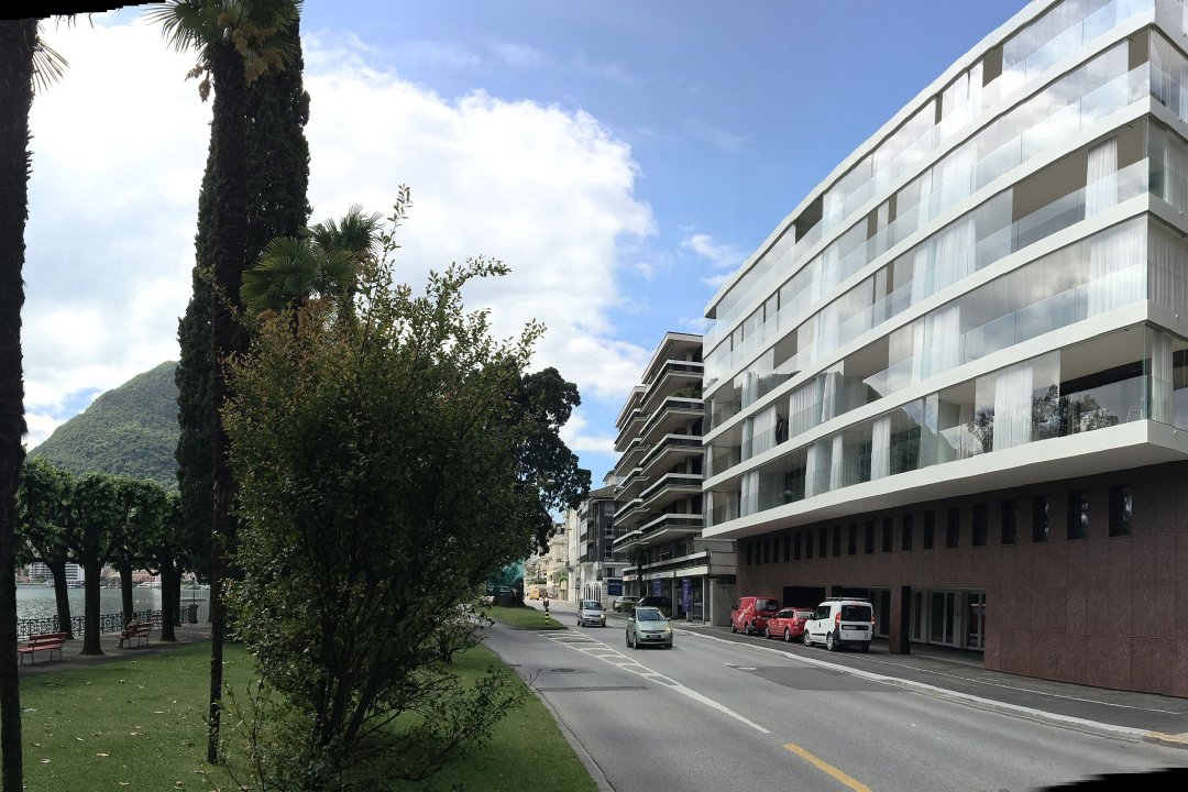 Immeuble de plusieurs étages aux balcons vitrés, le long d’une promenade au bord du lac bordée de palmiers