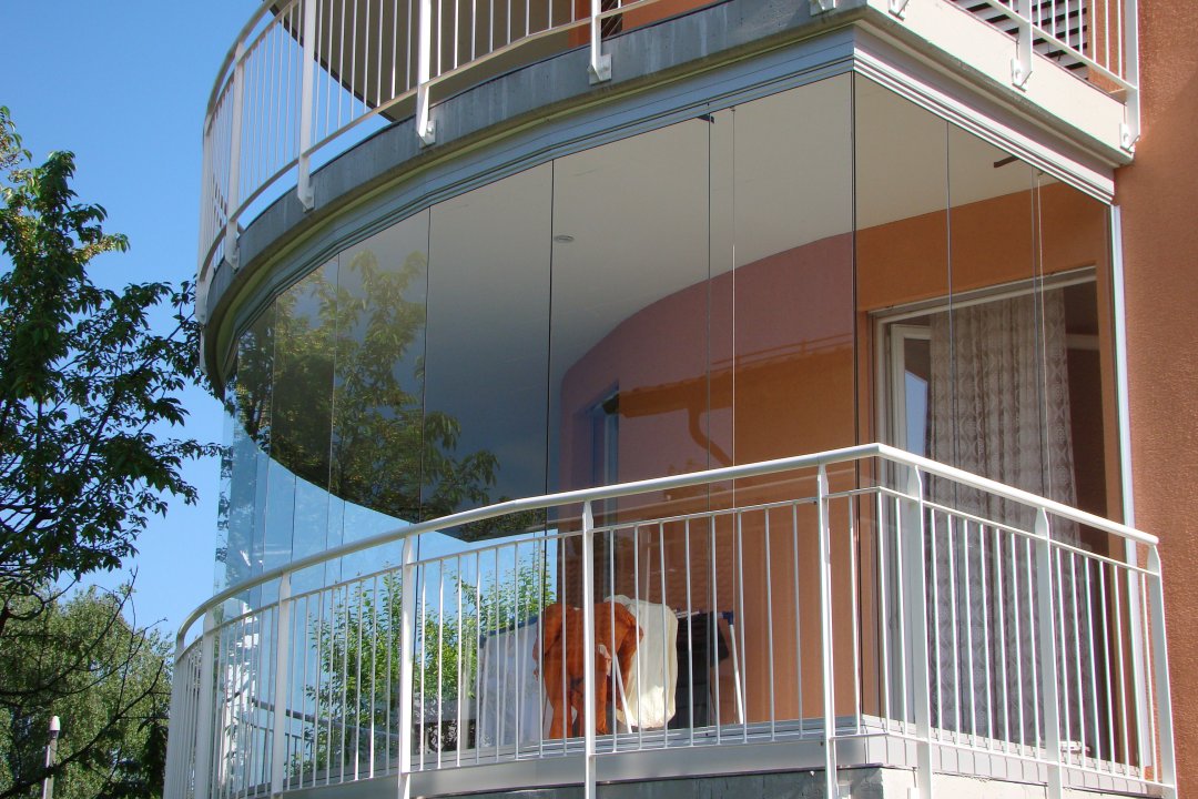 Vitrage de balcon arrondi sur un immeuble d’habitation avec garde-corps métallique blanc