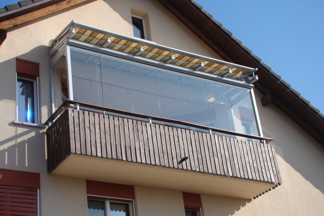 Vitrage de balcon avec garde-corps en bois et store banne sur la façade pignon d’une maison d’habitation